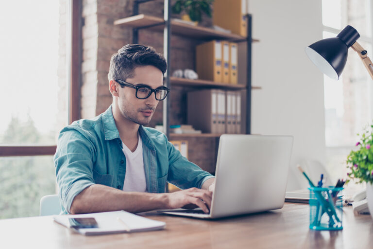 Young handsome minded man in jeans shirt typing in the laptop